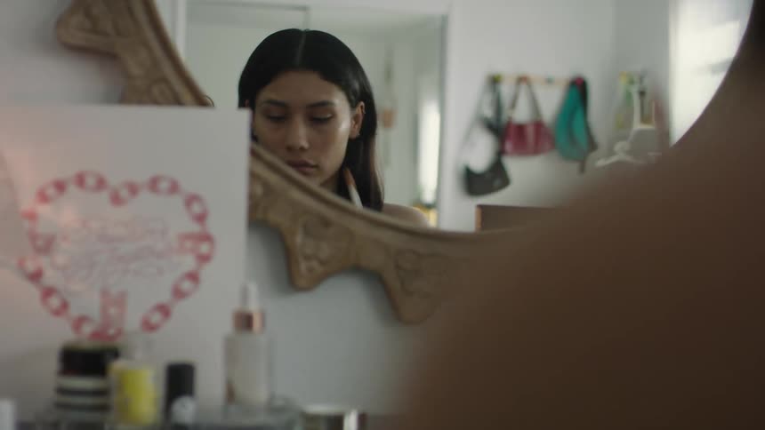 Young woman applying makeup in front of a mirror at home