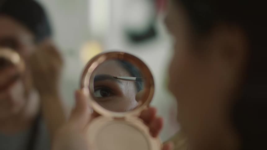 A woman is using a mirror to apply makeup