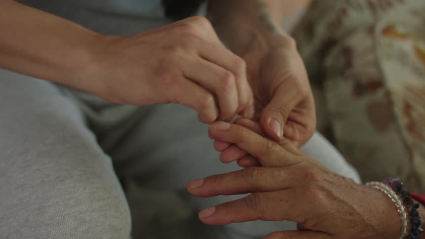 A woman is cleaning the fingernails of an elderly person