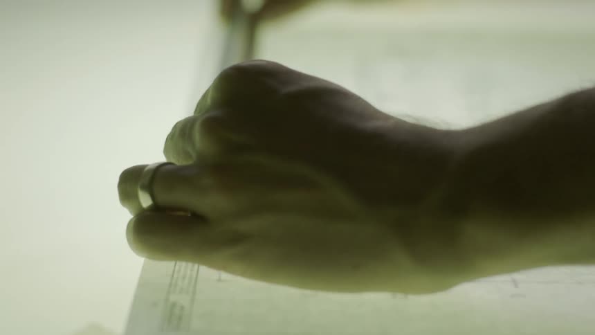 A man uses a ruler and make marks on paper