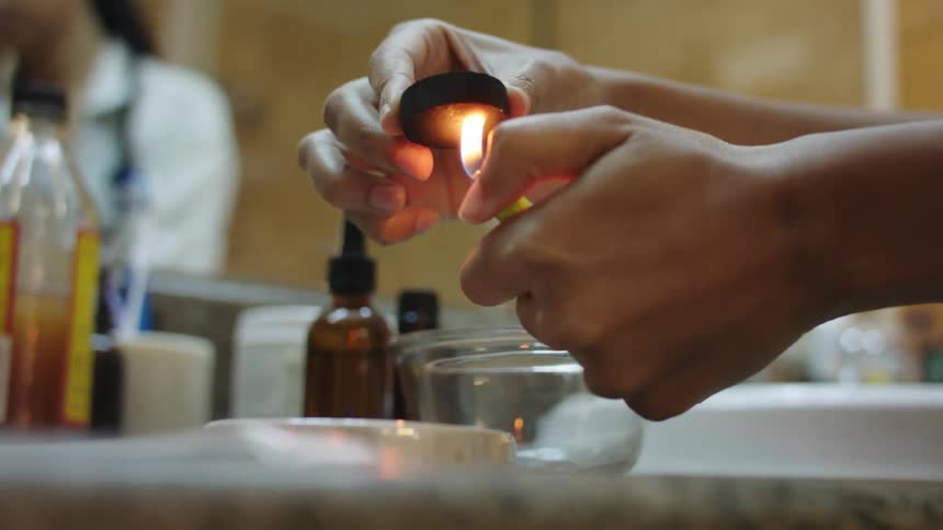 Woman uses a lighter to fire a round charcoal puck for burning incense over a counter top