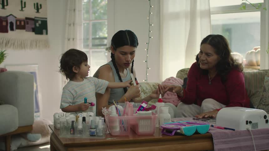 A woman is doing the nails of another woman and a little boy hands her some nail polish