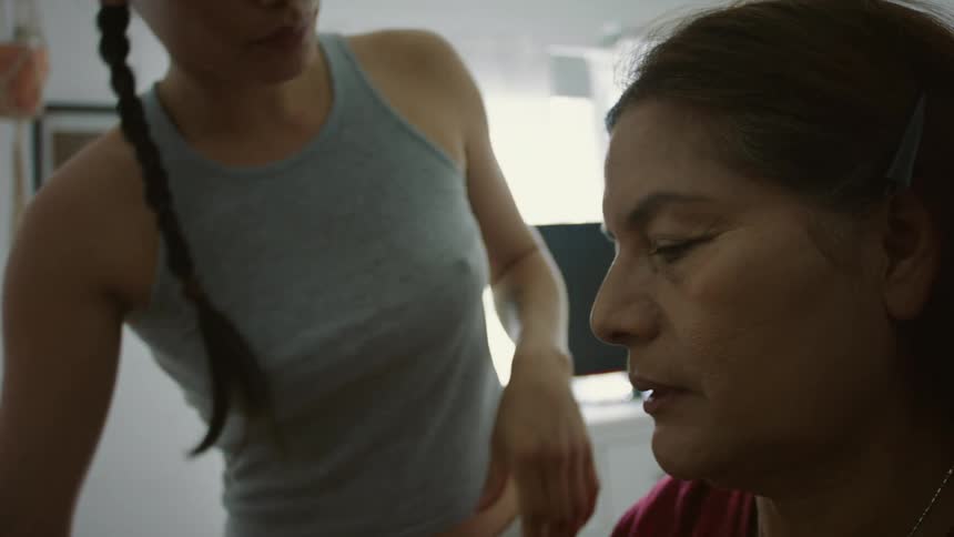 A daughter applies makeup to her mothers face in a white room