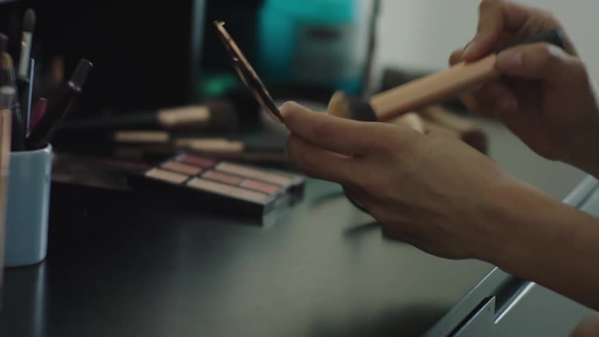 A woman is dabbing a makeup brush in a compact when a child hands her something