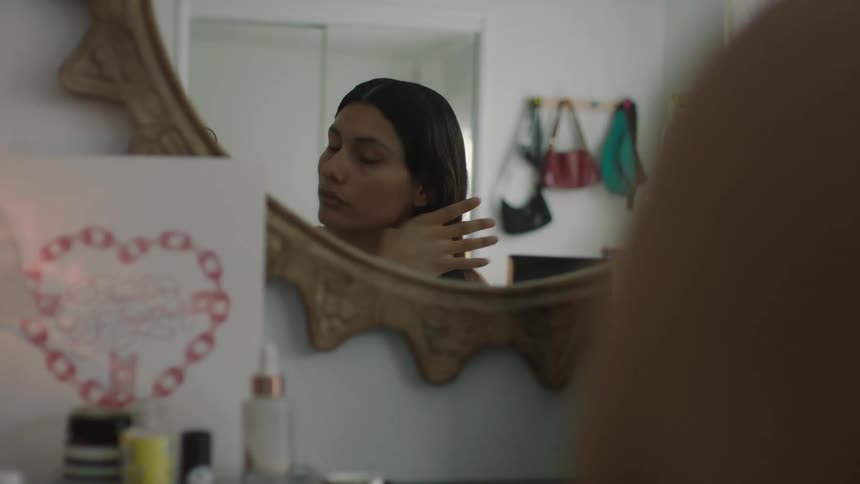 A woman applying makeup and styling her hair while sitting at a vanity