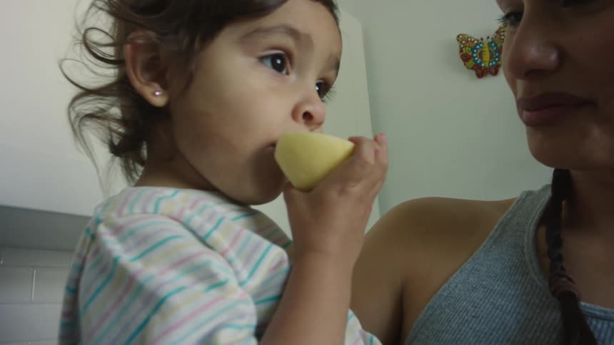 Toddler eating a lemon while being held by her mother in the kitchen