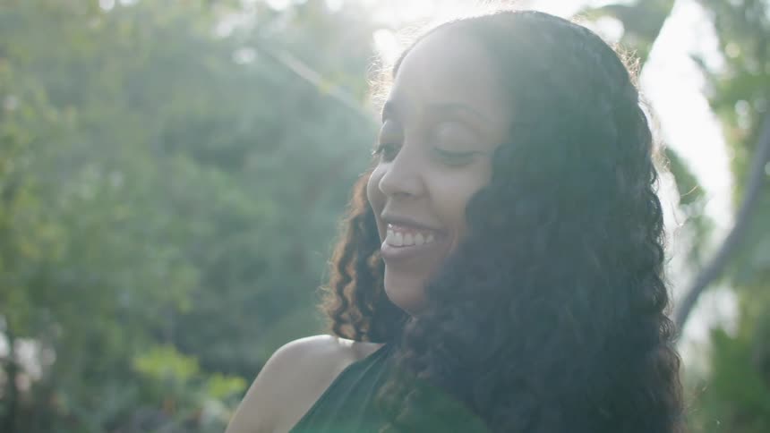A teenage girl is outside smiling and laughing as the sun shines on her