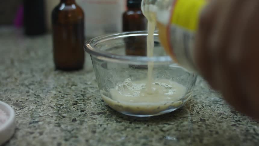 A person is pouring vinegar into a bowl with powder in it