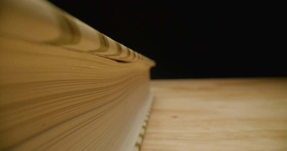 Extreme close up of the fore edge of a closing book resting over a wooden table