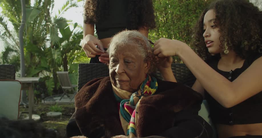 A group of people are sitting outdoors together and styling hair