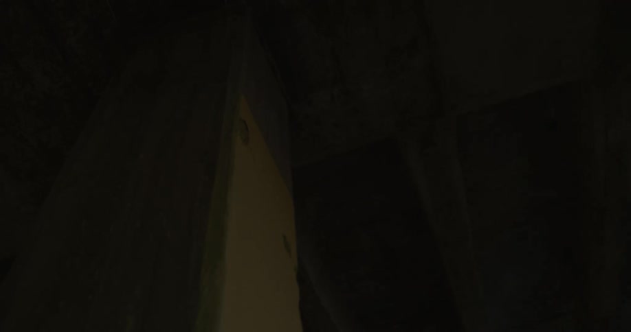 A light flashes in the dark illuminating a concrete column and ceiling beams with pipe