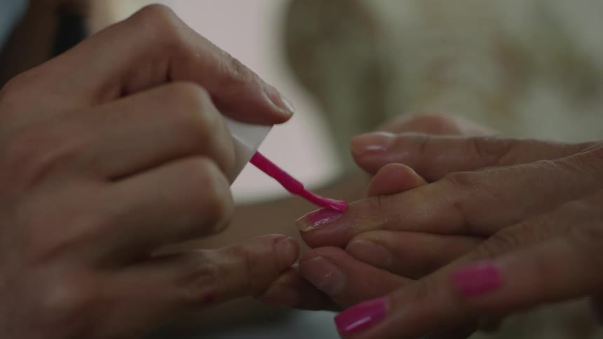 Woman applies polish to another persons fingernails