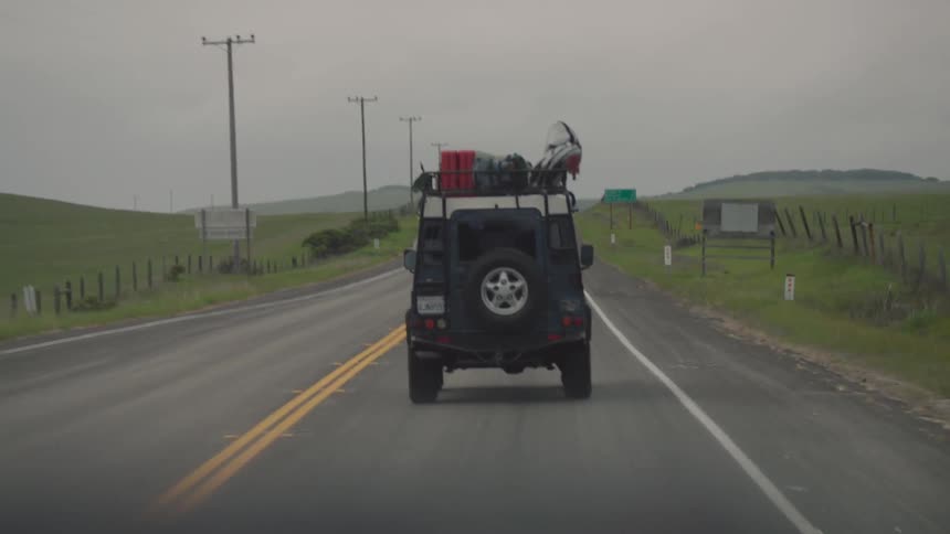 A vehicle carrying luggage on top rides down a road on a cloudy day