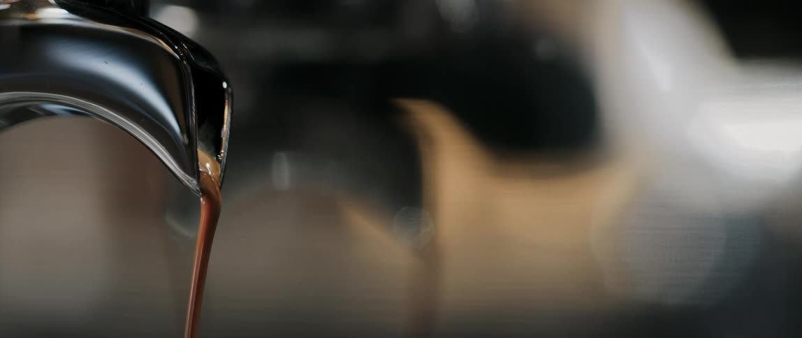 A shot of espresso is poured from a chrome coffee maker spout at a cafe