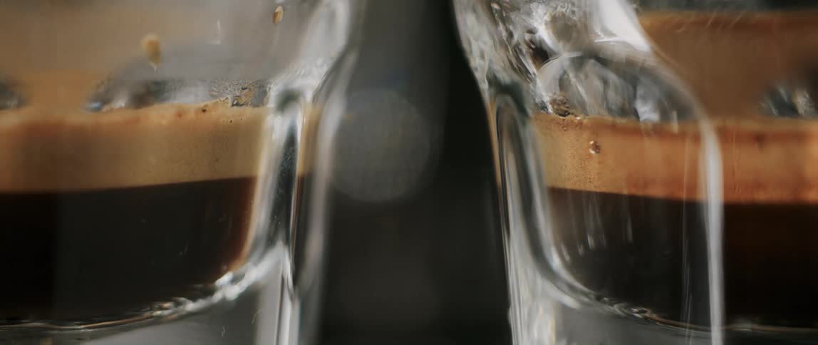 Close-up of glasses slowly being filled with frothy espresso coffee at a cafe