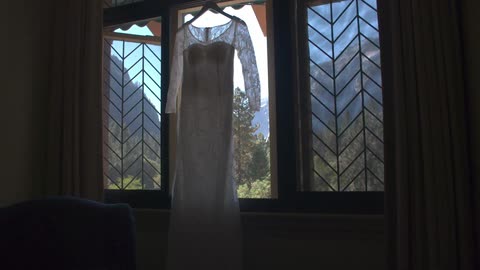 The camera moves toward a white lace dress hanging in an open window