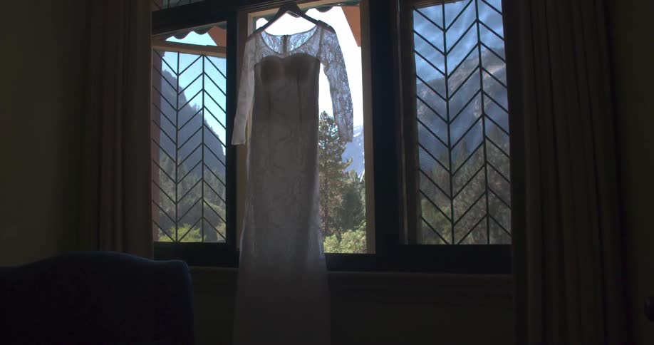 The camera moves toward a white lace dress hanging in an open window