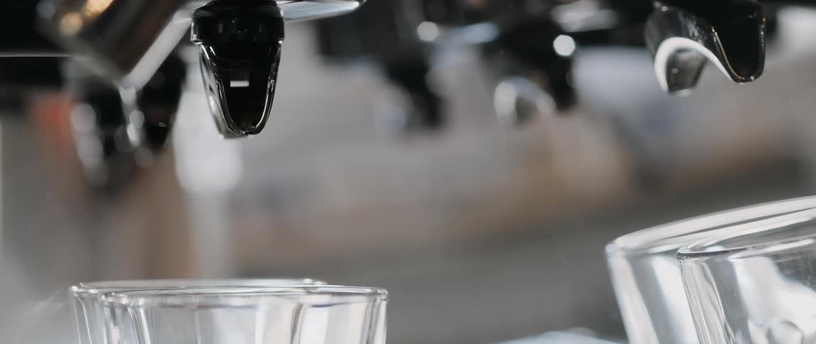 A barista prepares machine spouts to pour coffee into glasses at a cafe