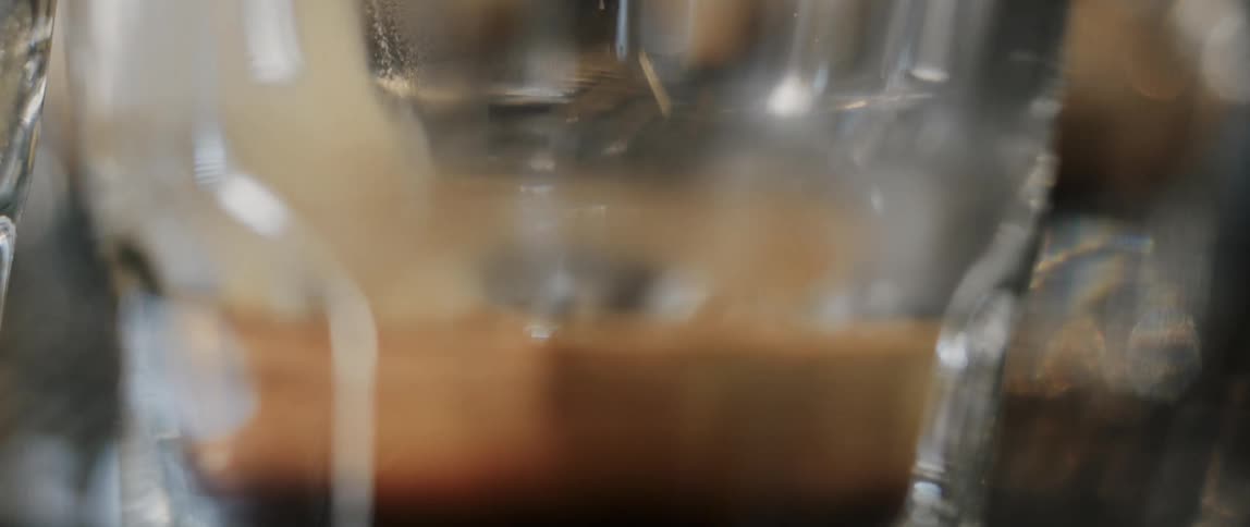 A hot frothy coffee drink being poured into a glass at a cafe