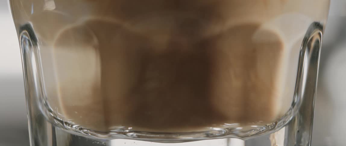 Brewed espresso coffee is poured into a glass of steamed milk to create a latte at a cafe