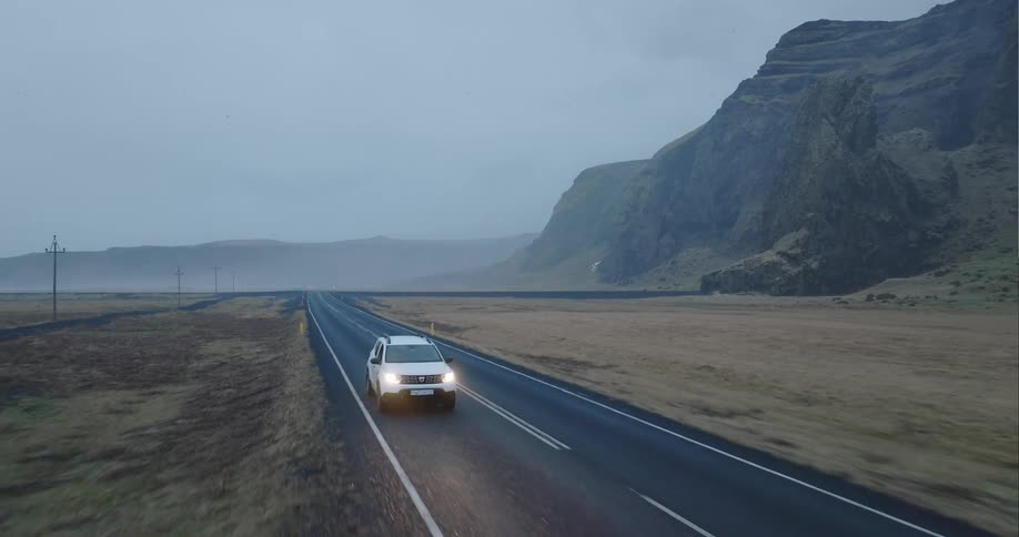 A white suv travels on a wet road on a foggy day
