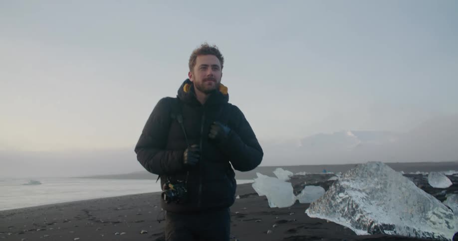 A man walks on a beach covered with large chunks of ice