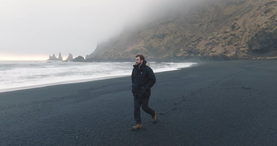 A man is walking on the beach near a body of water