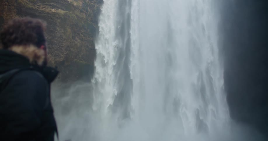 A man in a heavy coat watching a waterfall in nature