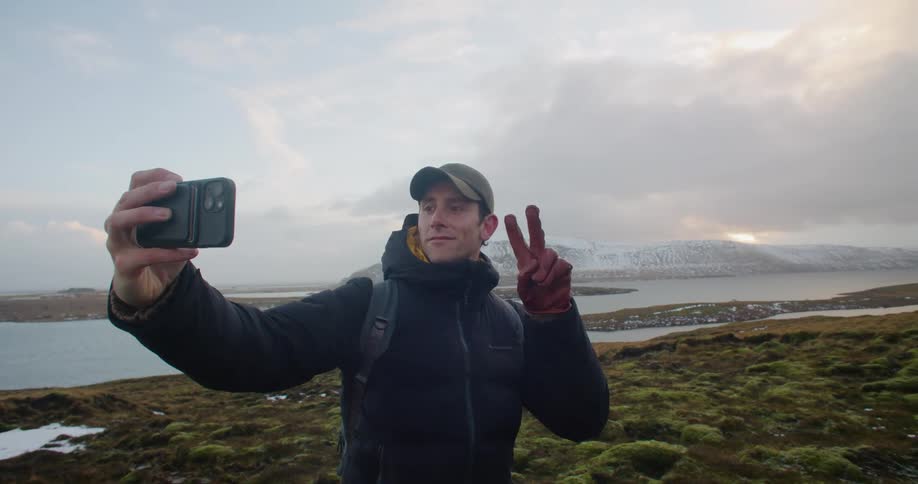 Young man travelling the countryside takes a selfie in front of the coast at sunset