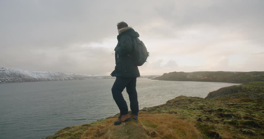A man hiking next to a lake in nature on a windy winter day