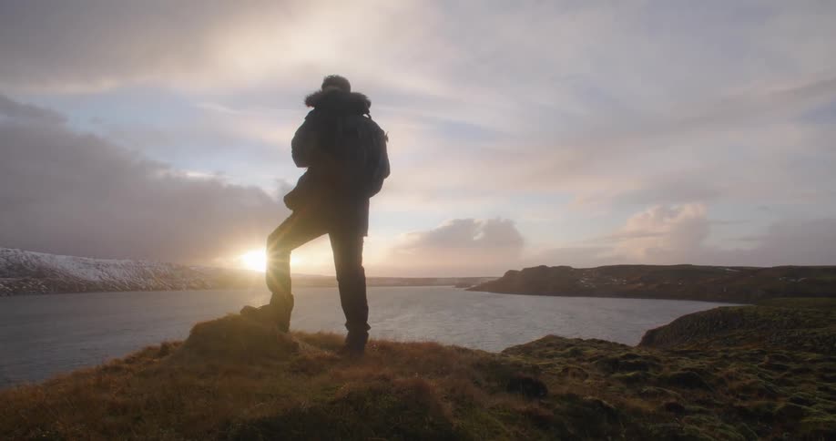 A man is standing outdoors and watching the sun set in the horizon