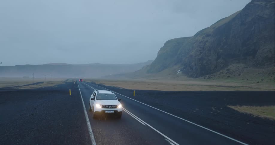 Aerial view of a white car entering a rural road near the mountains behind the distant fog