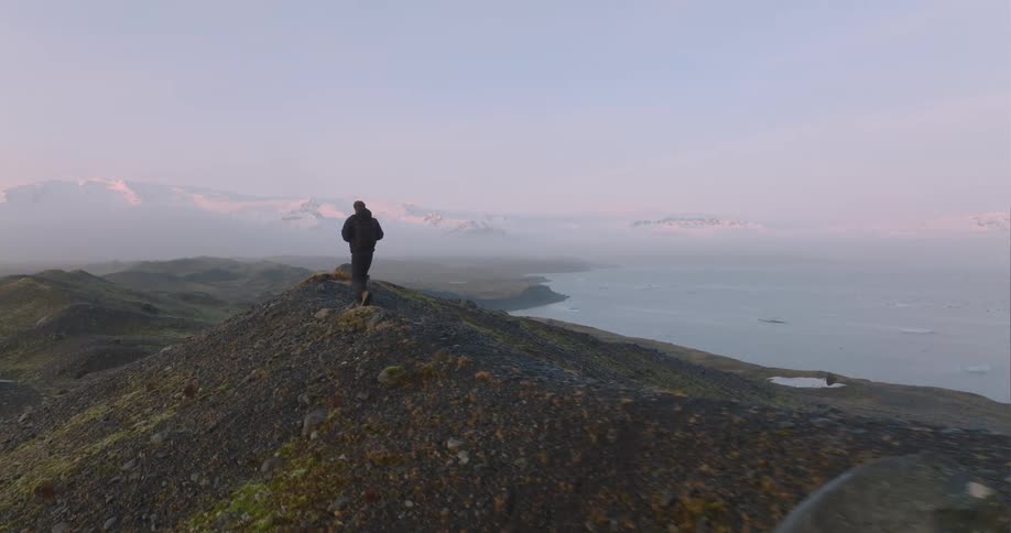 A man walks along a ridge high above the ocean coast