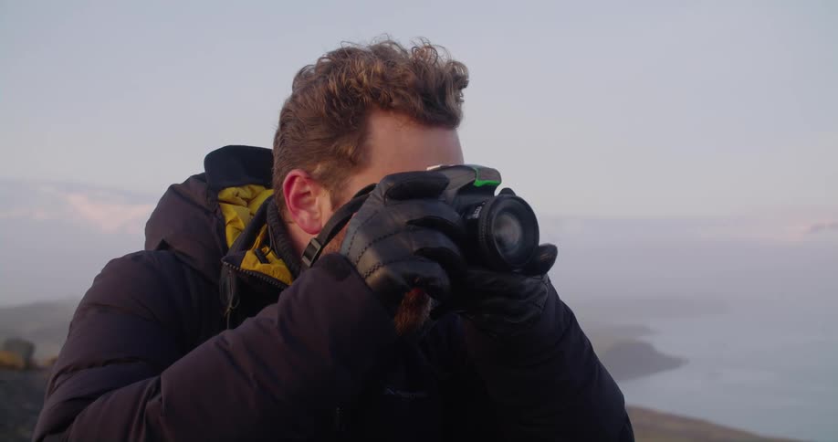 A photographer is standing on a cliff overlooking a body of water and taking pictures