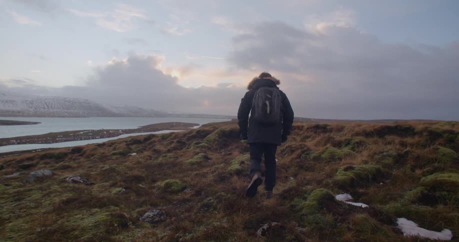 A man hikes over the grassy terrain on the shore