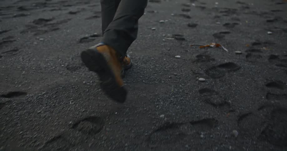 Young man walking among the footprints on the reynisfjara black sand beach at sunset