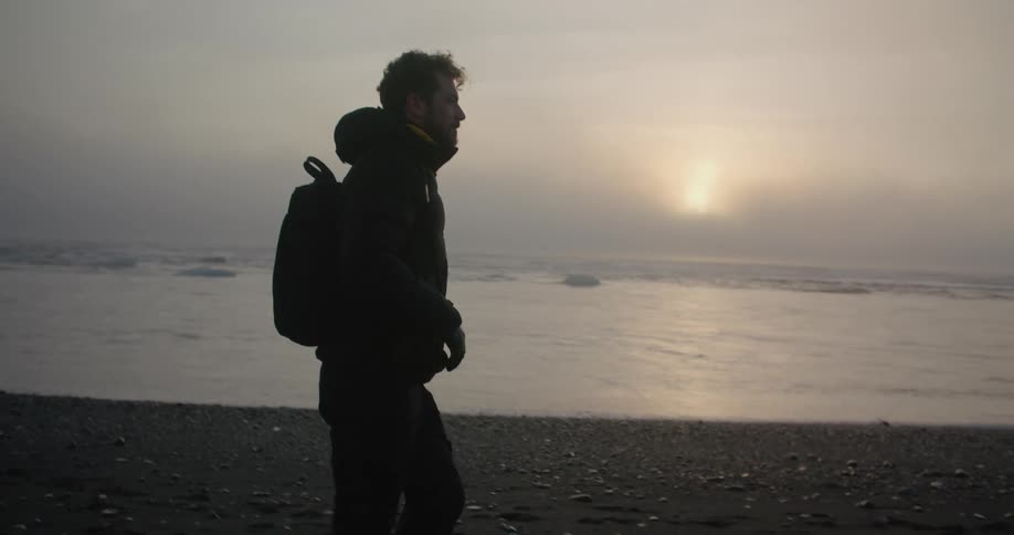 A man is walking on the coast near the ocean at dusk
