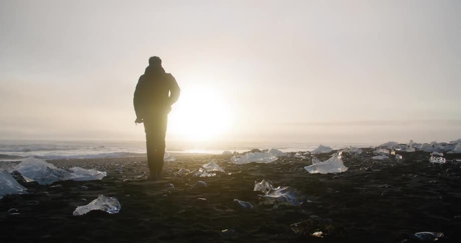 A man walks toward the ocean waves passing blocks and chunks of ice on shore