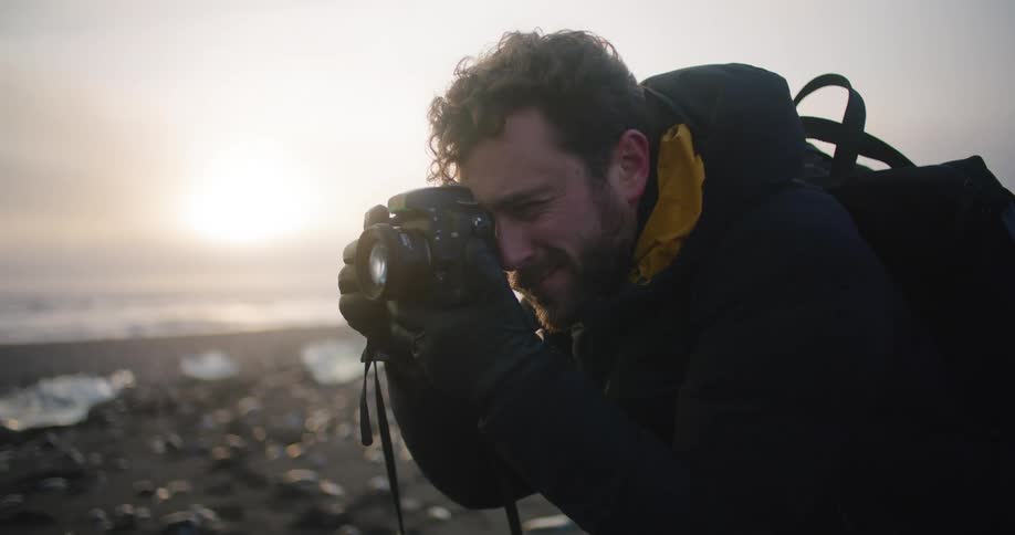 A man is on the coast of a beach and taking pictures