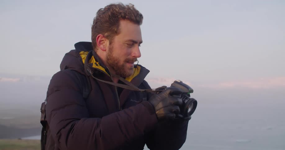 Young man takes pictures of the horizon near the reynisfjara black sand beach at sunset
