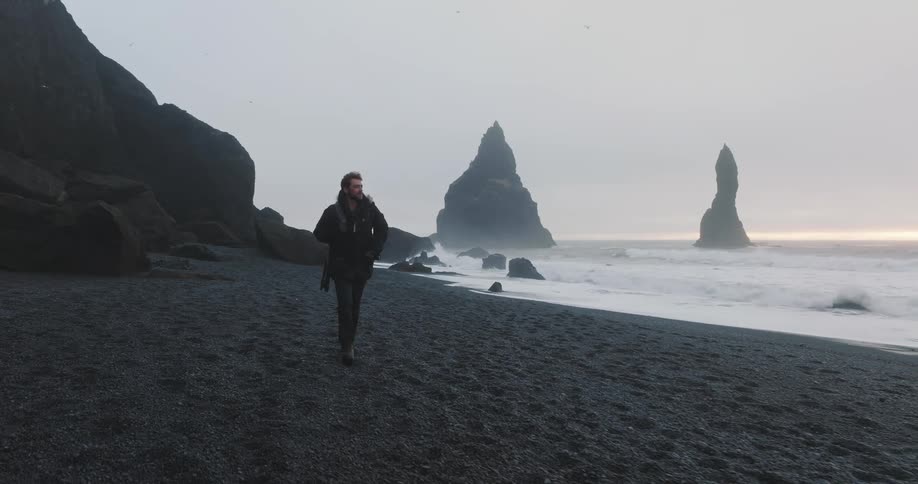 A man is walking on the coast of a beach at dusk