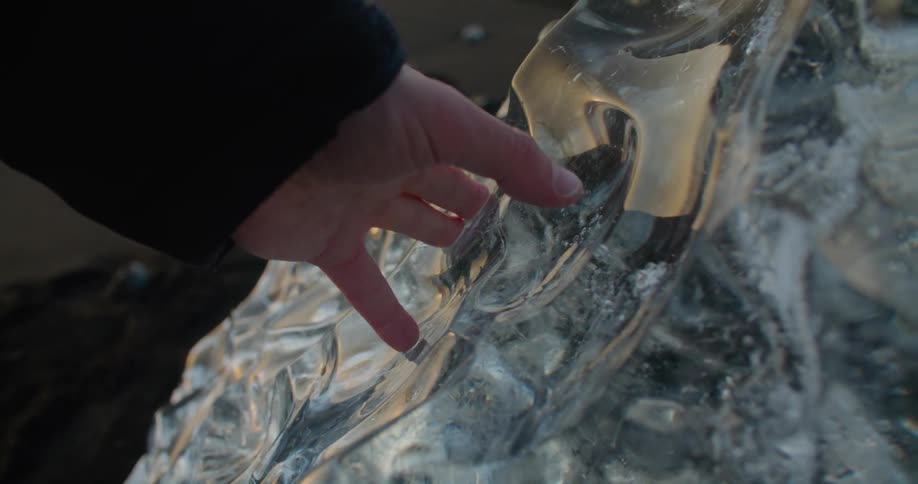 Man touching a natural block of ice over the reynisfjara black sand beach at sunset