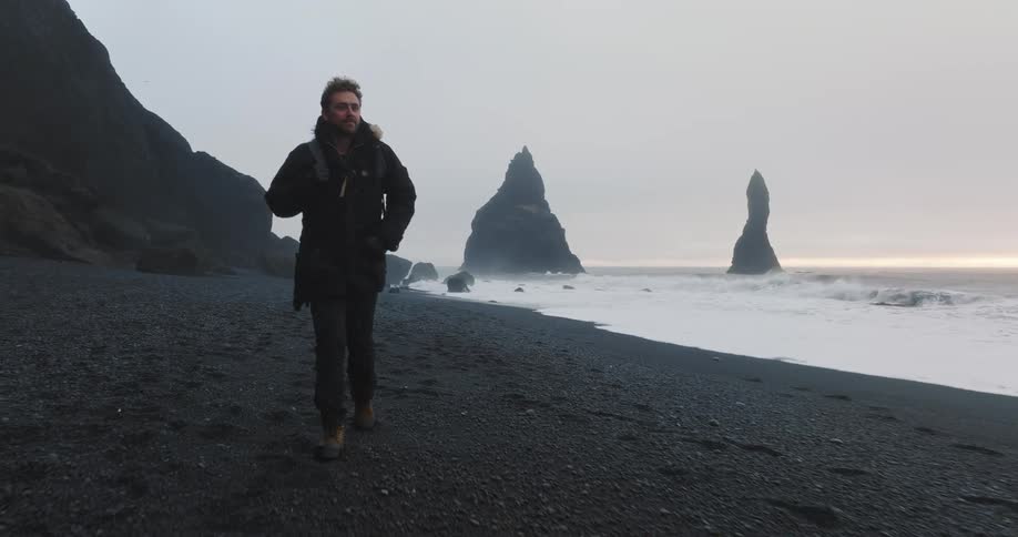 A man is walking alone on the coast of a beach at dusk