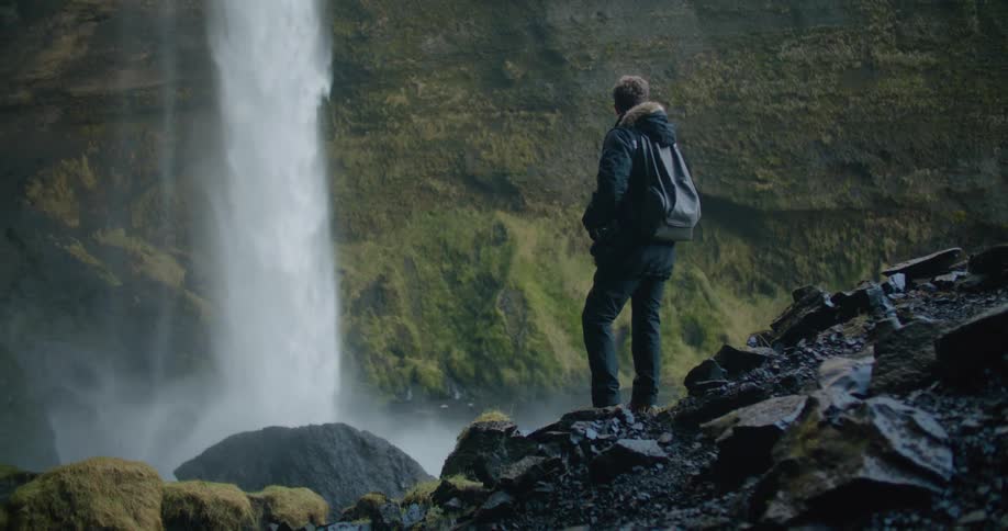 A man is standing outdoors and water a waterfall
