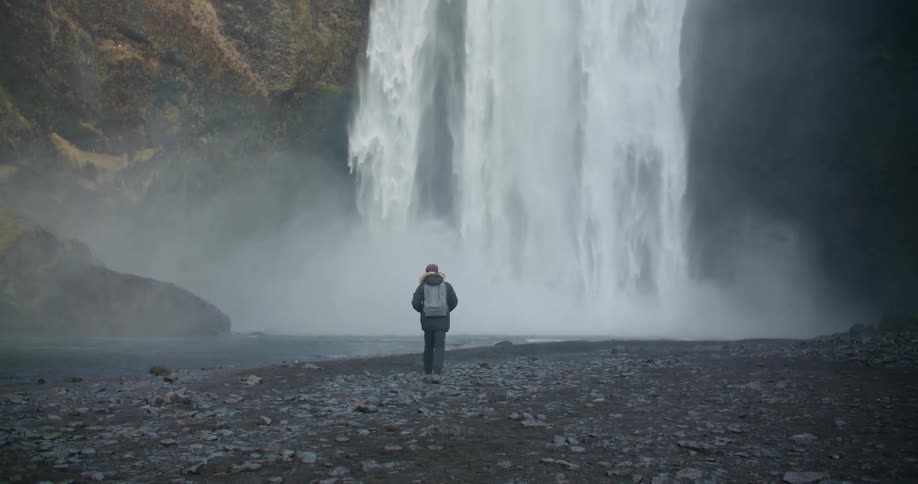 Young man walks towards a waterfall close to the reynisfjara black sand beach