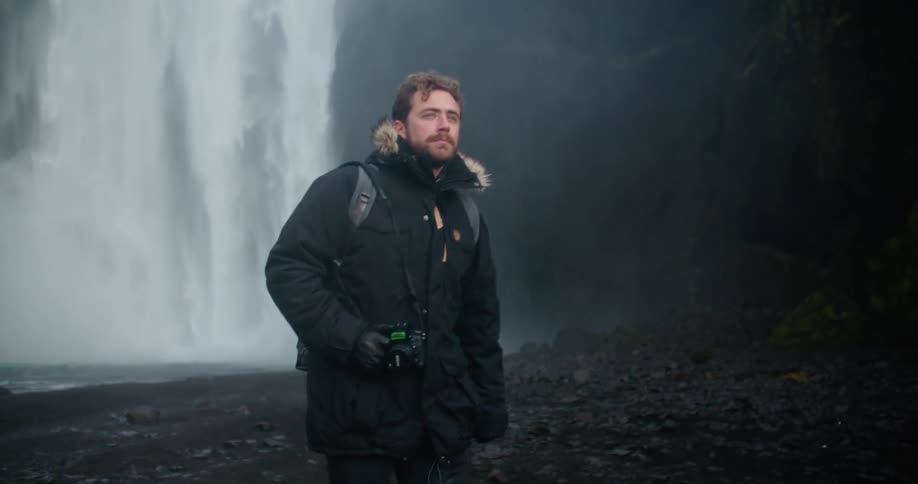 A man is walking away from a waterfall and holding a camera