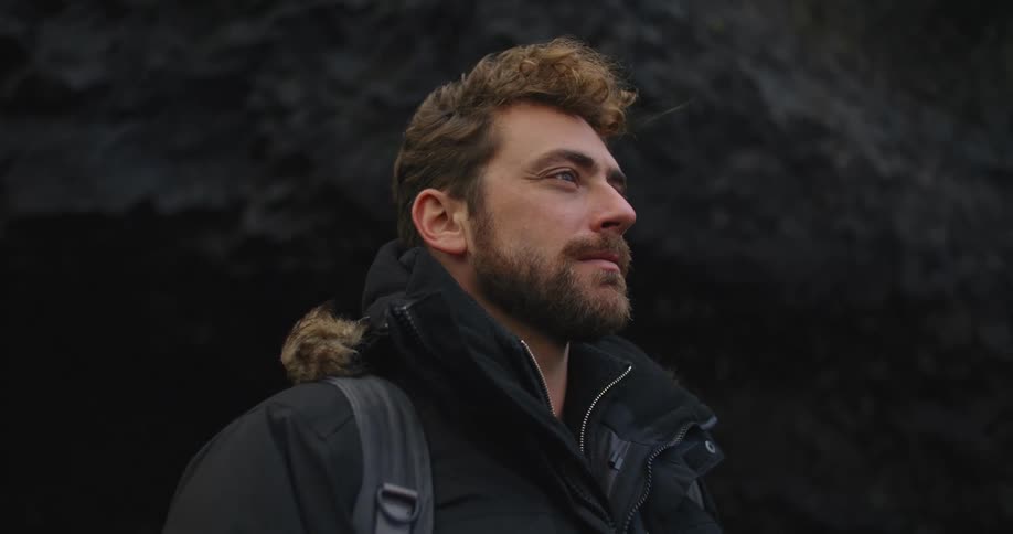 A man is standing outdoors by a cliff