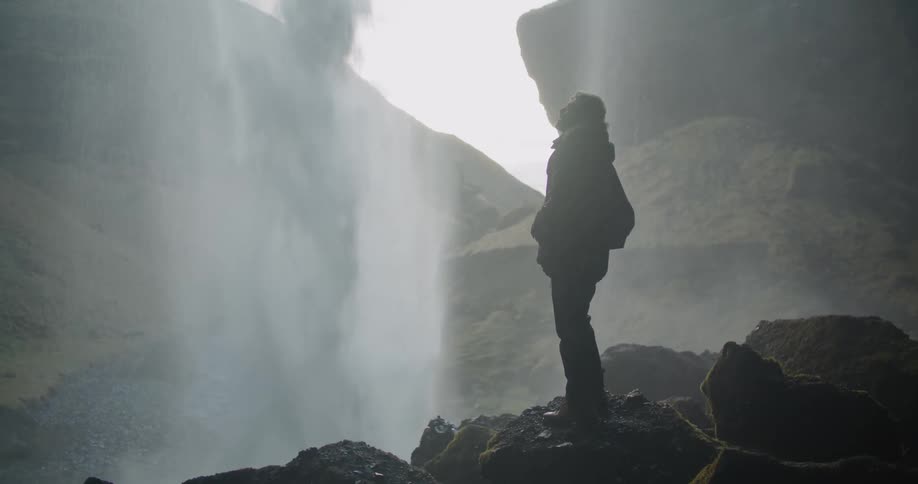 A man stands on a rock looking up in awe as water rushes and splashes down from above