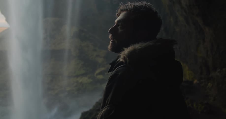 A man stands in the cave watching the waterfall