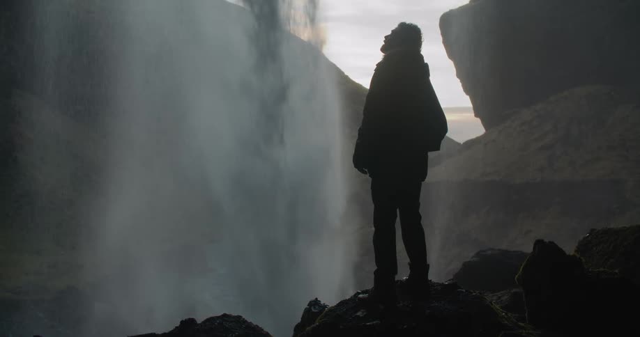 A man watches the waterfall from inside the cave